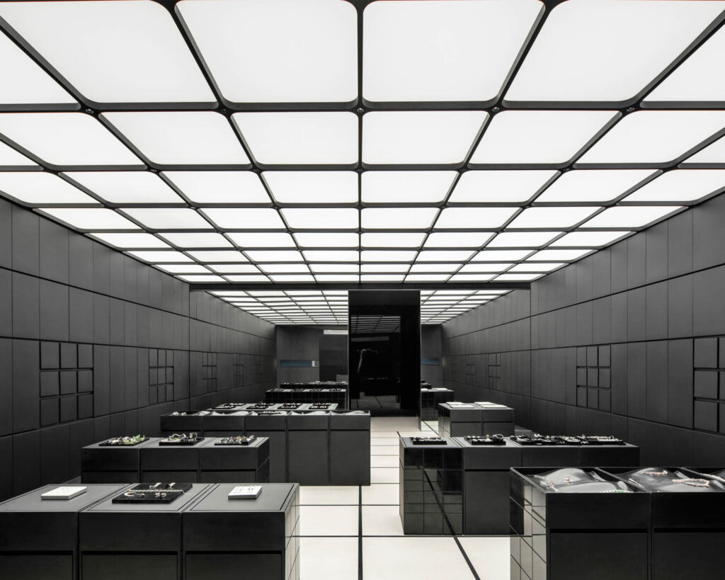 Black horizontal tables create a maze within the showroom lined with black walls and a grid pattern above and below