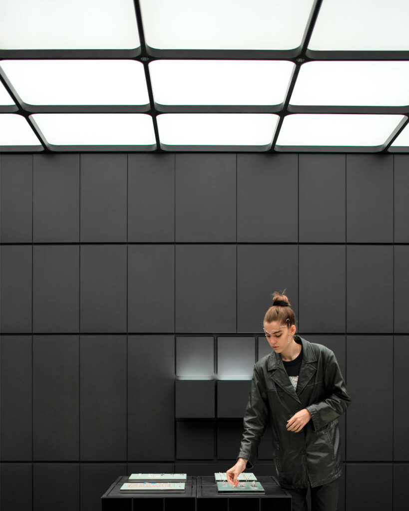 A woman looks at accessories on a black table near a black wall