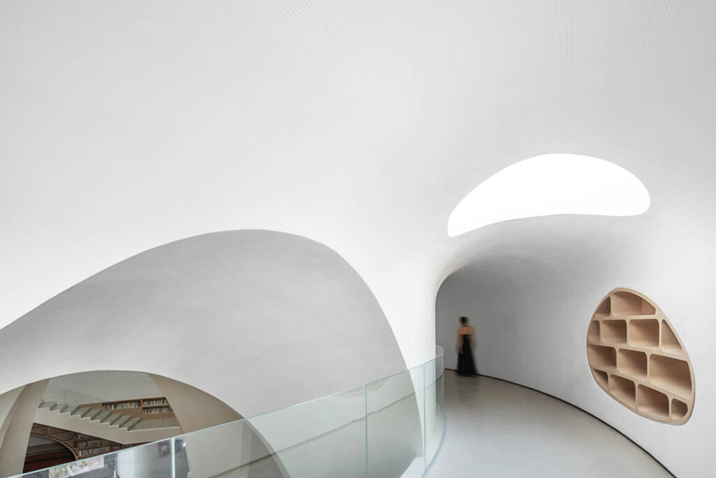 A woman in a black dress walks down a winding, cavelike white hallway 