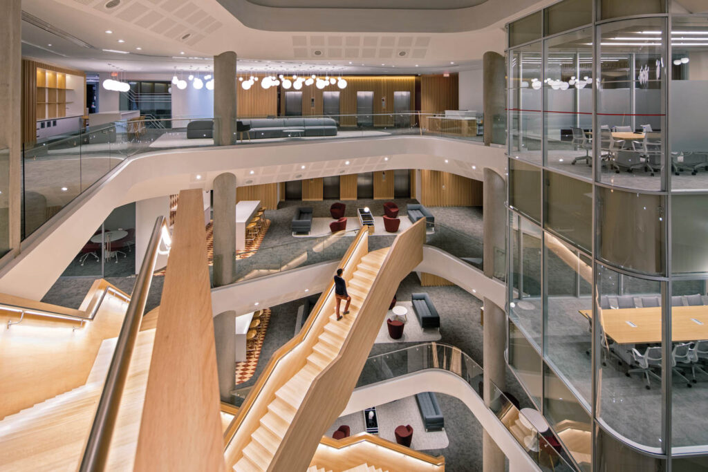 a man walks up brightly lit stairs in the center of an office building 