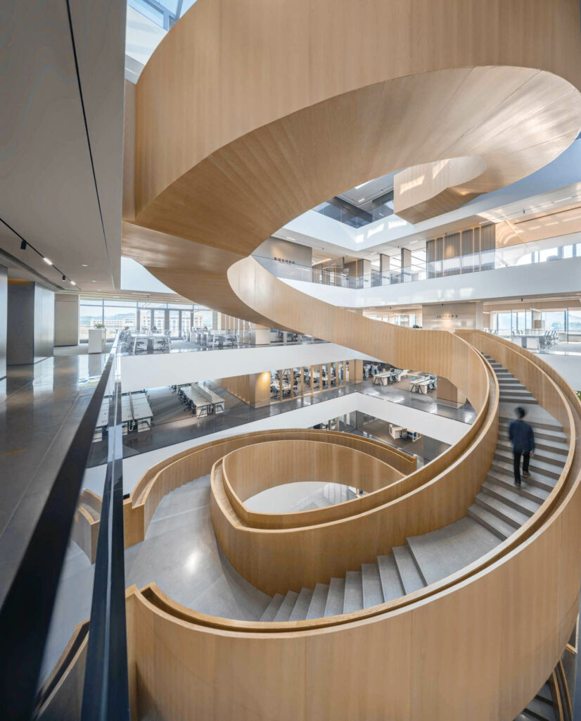 A wooden staircase with gray steps curves through the center of an office building.