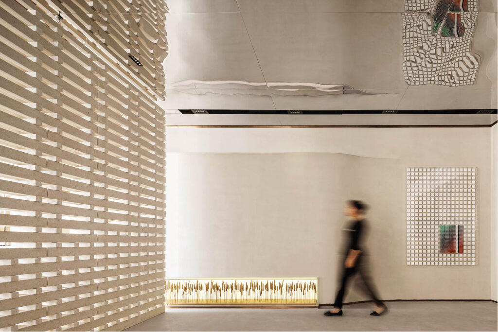 A blurred person dressed in black walked by an installation of wheat in a room with a mirrored ceiling. 