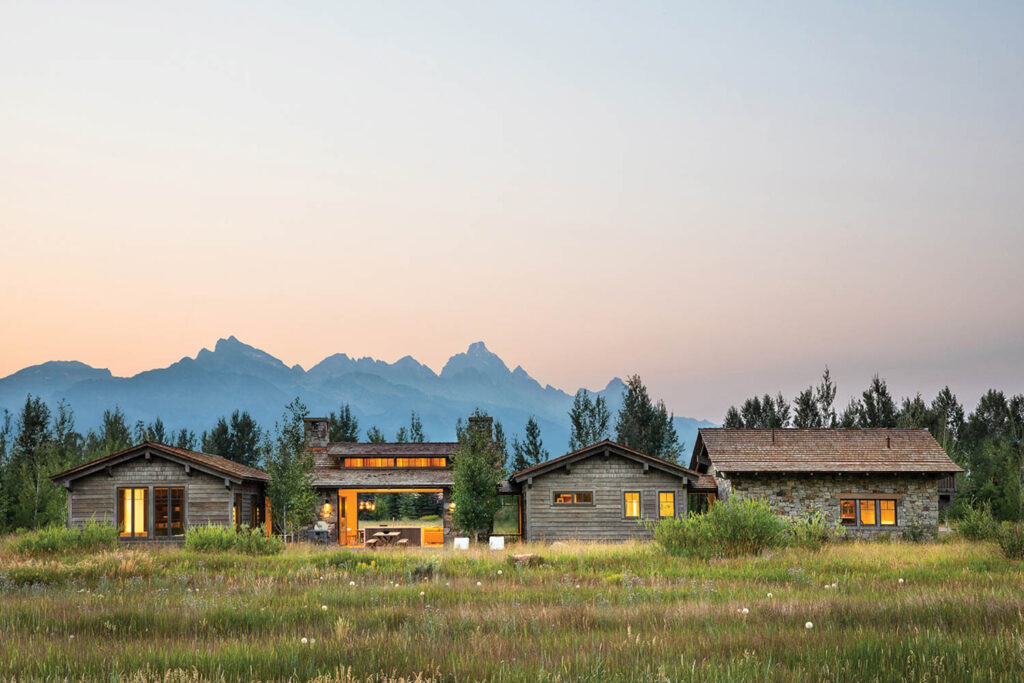 The exterior of a mountain retreat at dusk surrounded by wildflowers with mountains in the background.