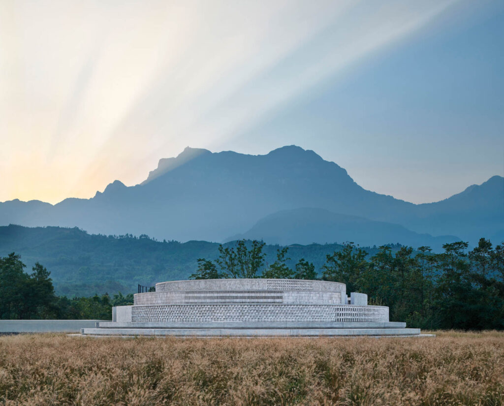 a partially underground rotunda made of concrete bricks with mountains in the distance