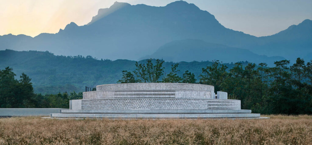 a partially underground rotunda made of concrete bricks with mountains in the distance