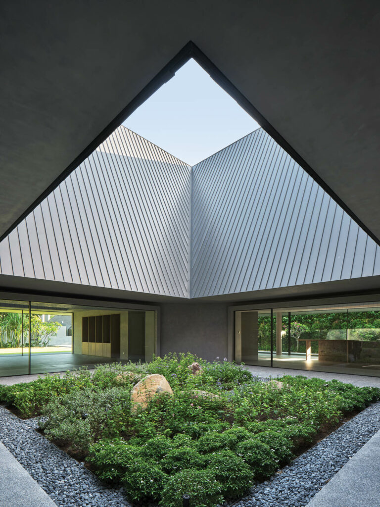 A pitched roof opens to reveal a courtyard with lush greenery and rocks