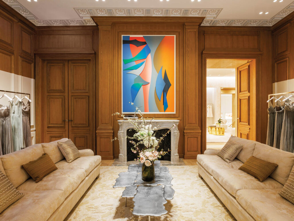 a silver coffee table sits in the middle of a luxurious room with a fireplace, large artwork at the center, and sofas on each side