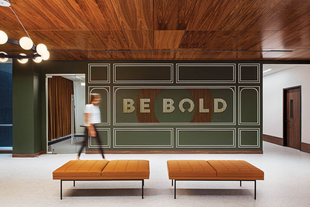 a person walks past a wall with Be Bold written on it behind seating benches