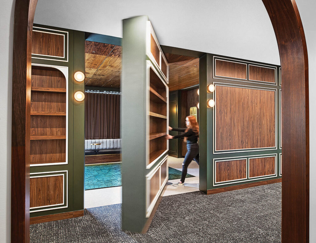 a woman opens a secret door in a wall of shelves