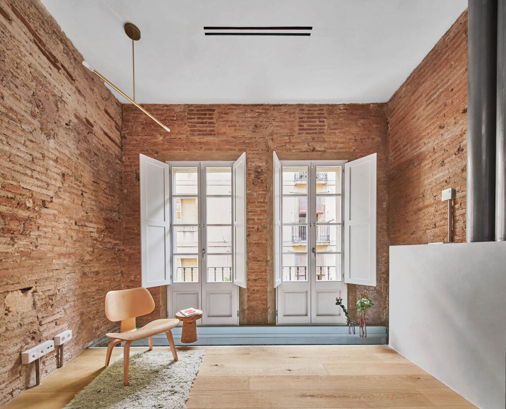 a living room with wood flooring and exposed brick walls, with large windows overlooking the balcony