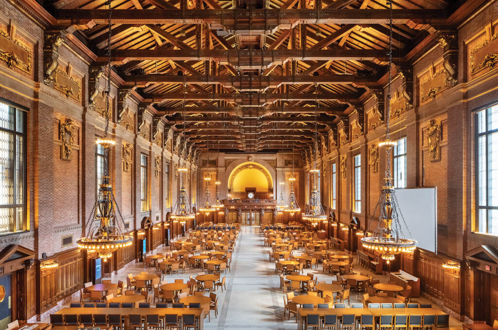 a grand room with tables for groups to sit at and large clock at the end of the room