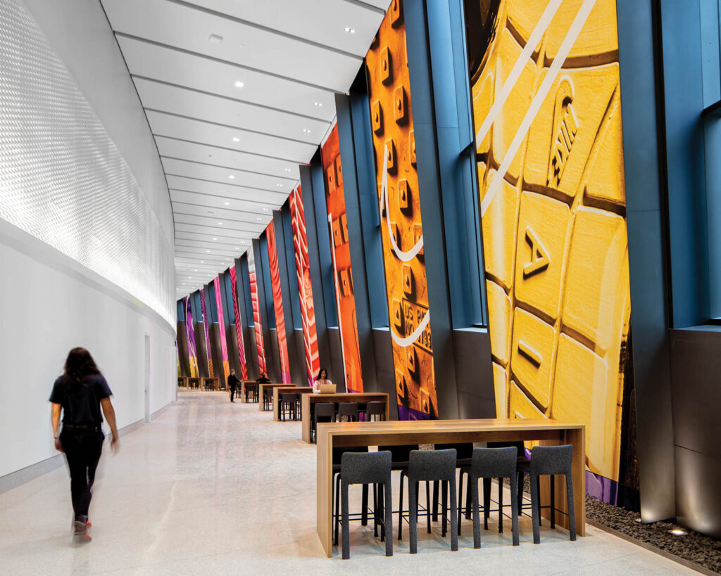 A woman walk down a curving hallways where bright graphics of sports gear details line the walls.