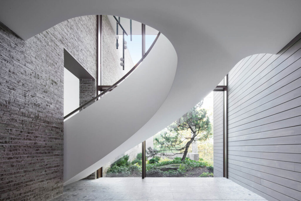 the underside of a white staircase in front of a glass wall with trees seen outside