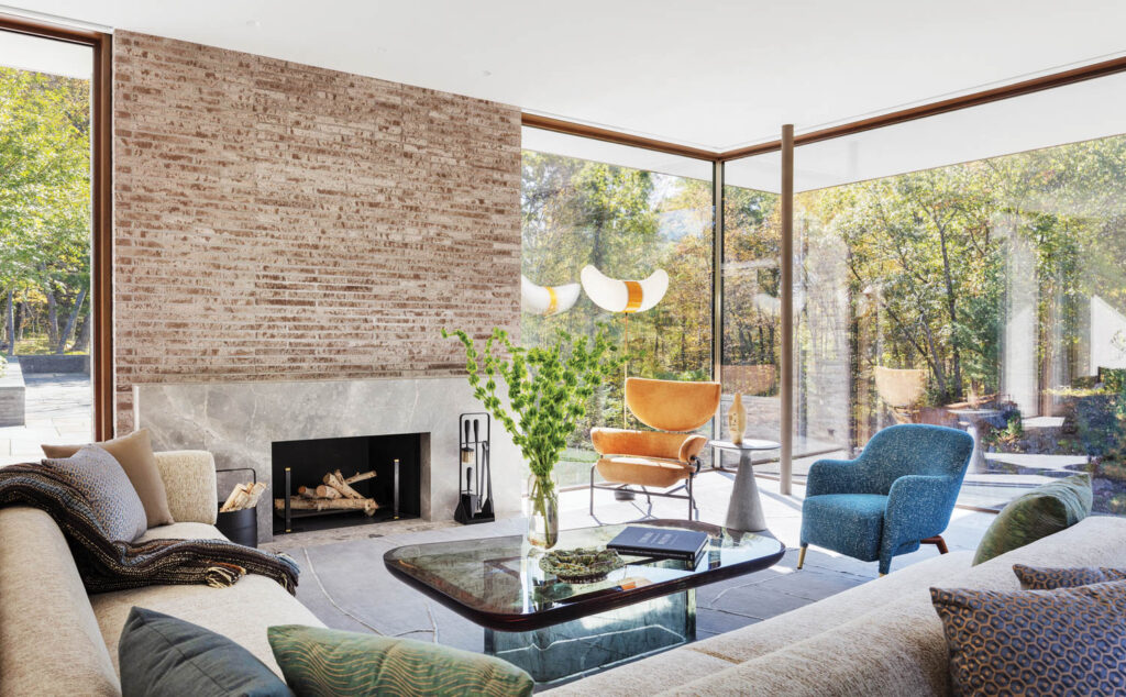 glass walls enclose a sitting room with a brick fireplace and cozy seating