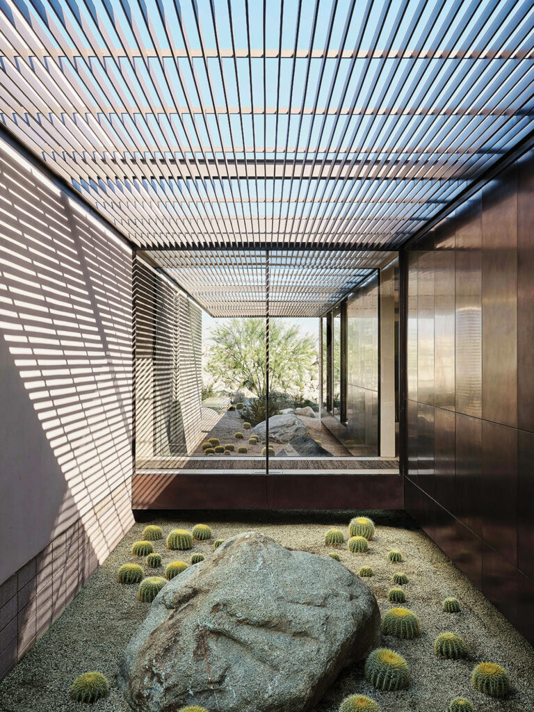 Cactuses and boulders are framed by an open-air metal grates forming an indoor-outdoor space.