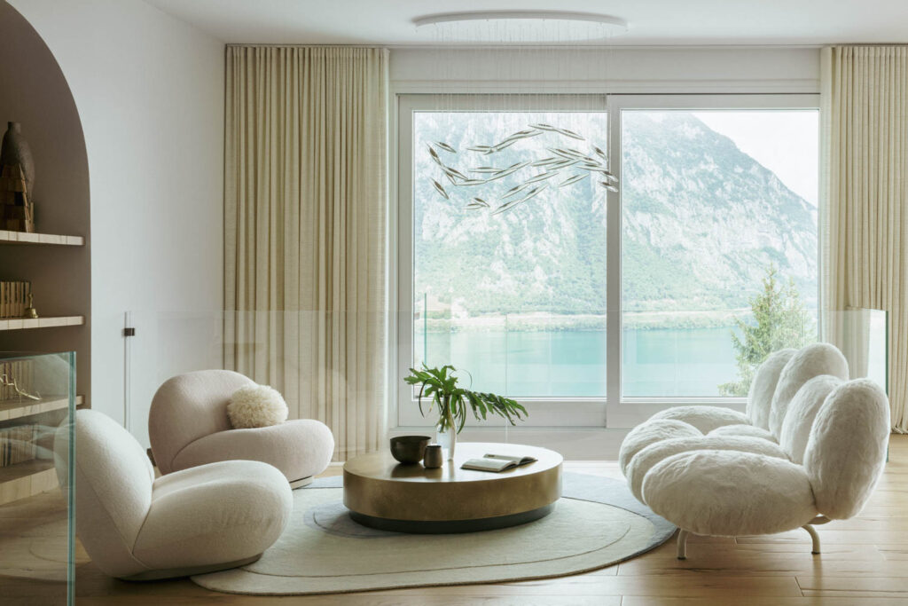 lounge chairs in a neutral living room sit in front of a window looking out over the water