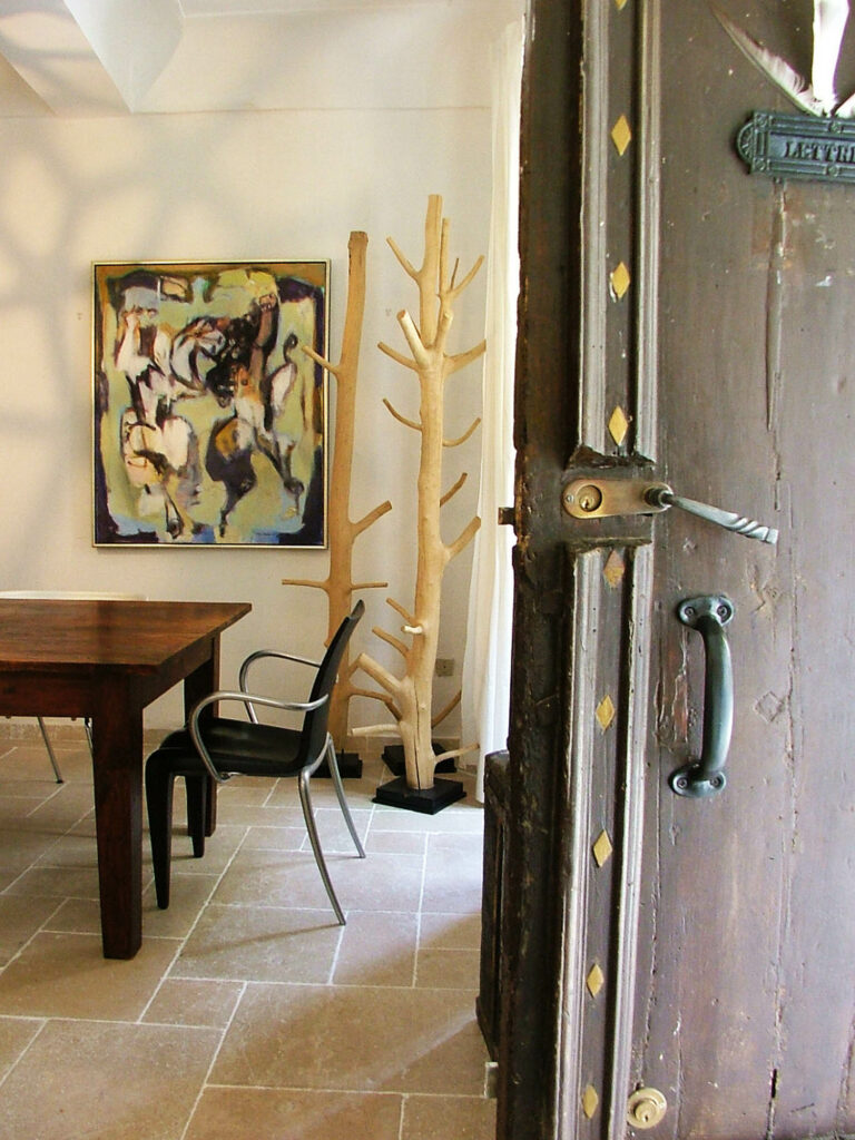 an abstract painting hangs on the wall of a foyer next to a tree-like coat hanger