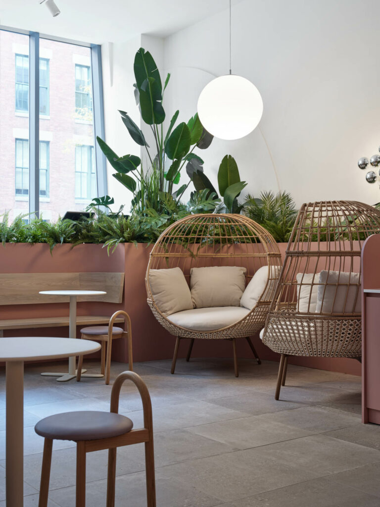 Wicker chairs with cream cushions in front of a ledge with greenery.