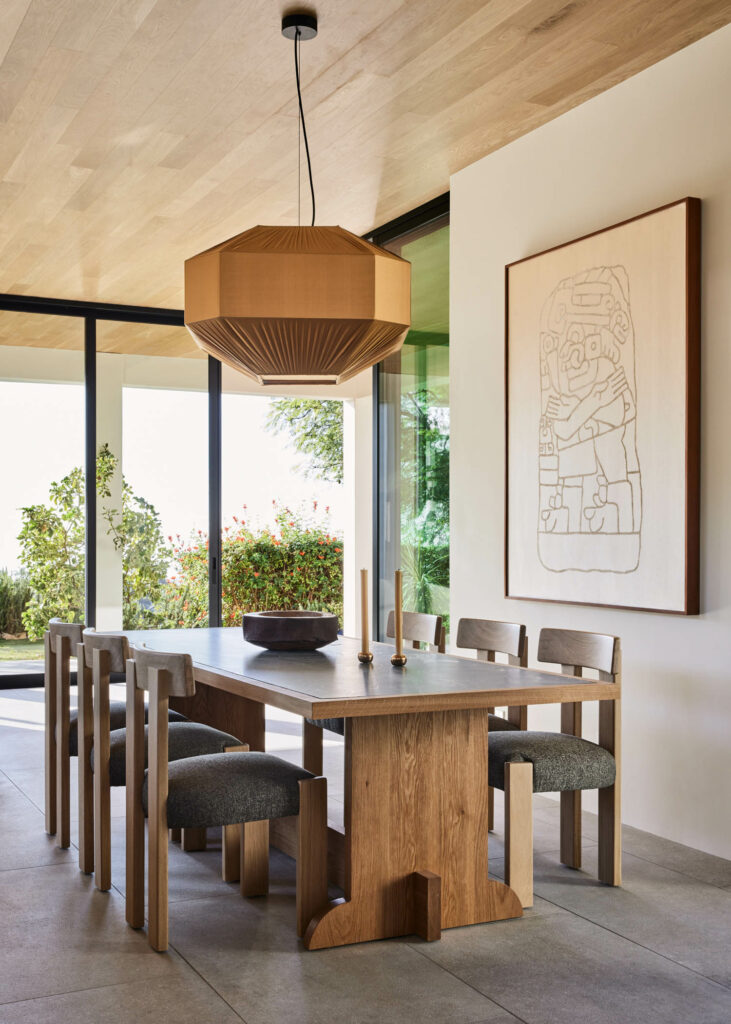 a dining room table beneath a honey colored pendant light and artwork by Gala Porras Kim