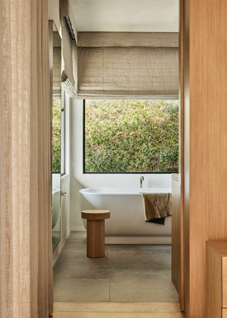 a primary bathroom in neutral colors with views of natural vegetation