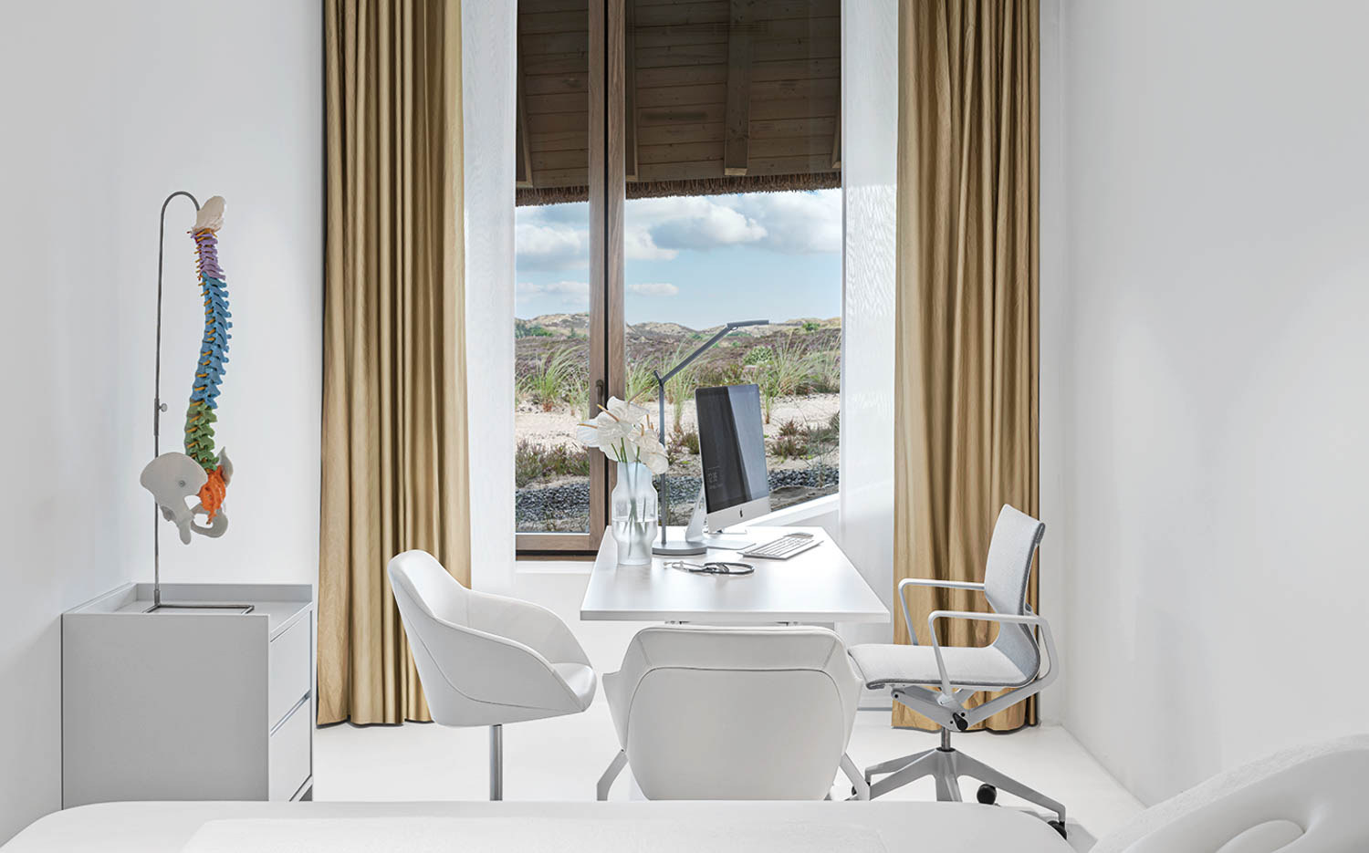 a medical office overlooking sandy dunes with an anatomical spine in the corner and white furnishings