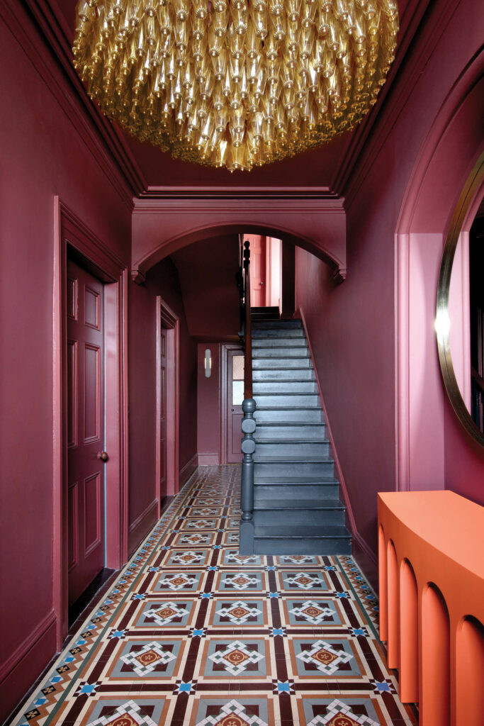 an entry hall with blue stairs, maroon walls, and a vintage glass chandelier