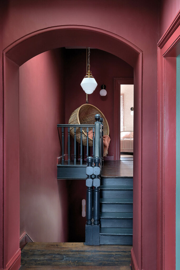 a hanging rattan chair at the top of the stairs under a pendant light