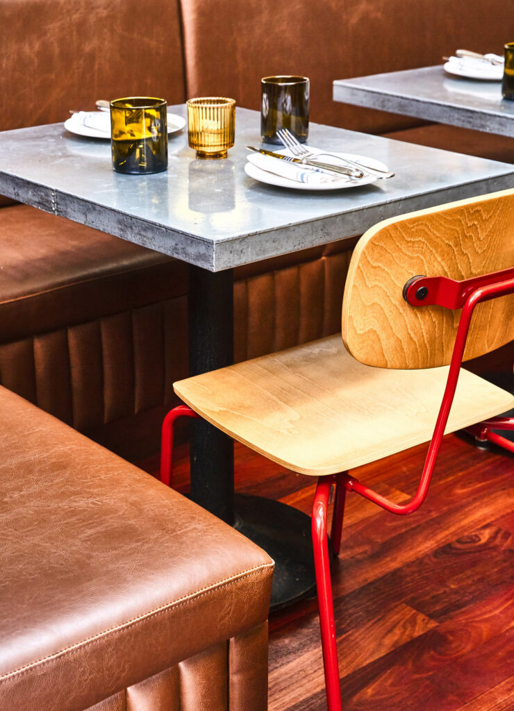 brown vinyl banquette seating wraps around the back of a grey table with a red and wood chair on the other side