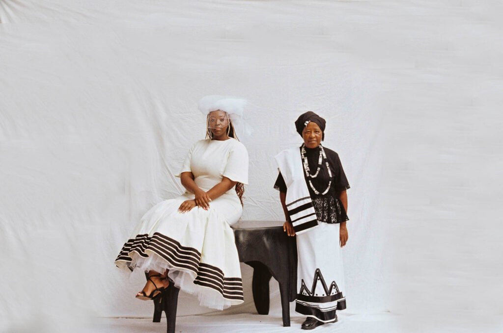 Thabisa Mjo and her mother wearing uMbaco dresses in black and white patterns sitting on a table. 