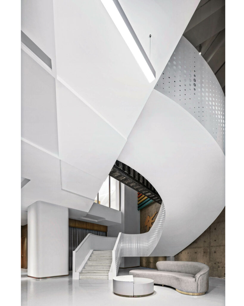 The underbelly of the white curving staircase frames a curved sofa and coffee table.