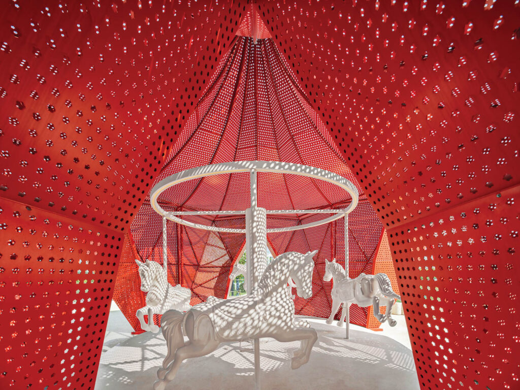 a carousel of white horses inside a red aluminum tent