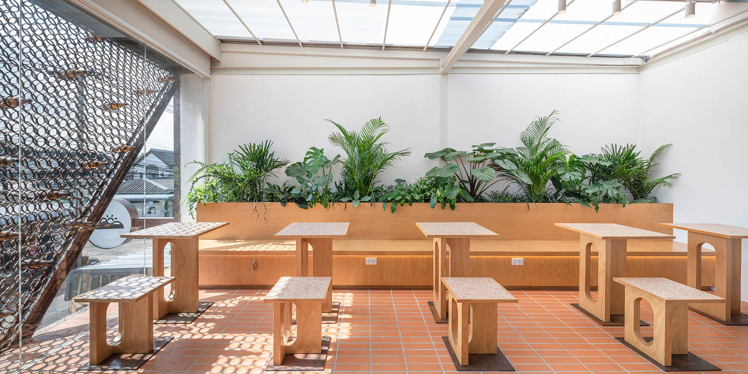 an open air floor of a coffee shop with greenery lining the wall behind seating