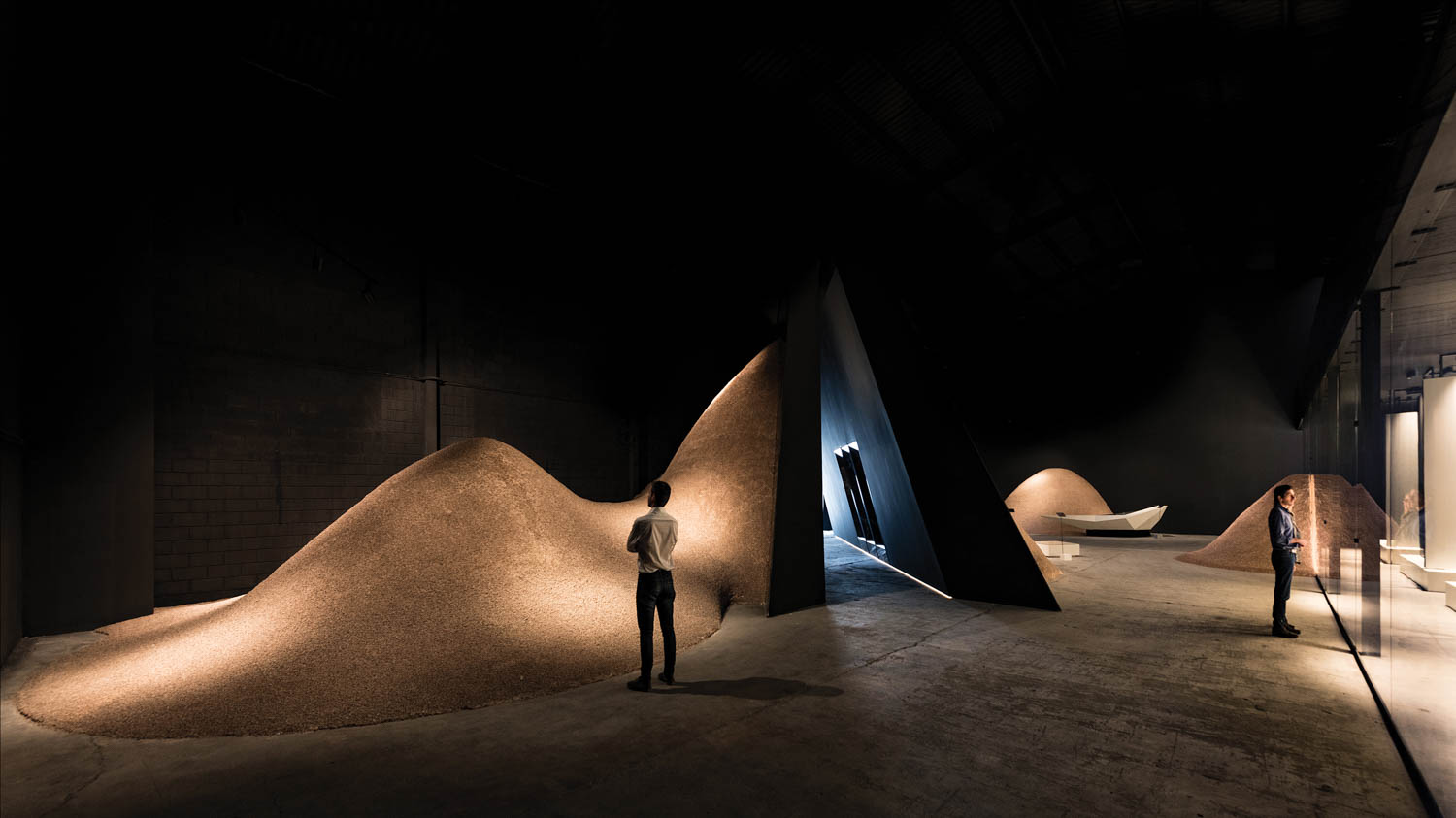 A person stands in a dark showroom next what appears to be sand dunes