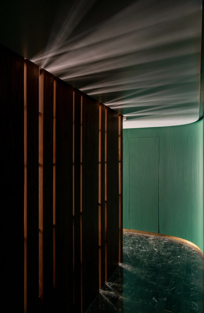 a dark green fluted wall opposite a teak wall in the entry foyer of a Mumbai apartment