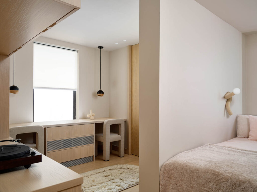 a bedroom with a partial wall separating the bed from a wall length desk