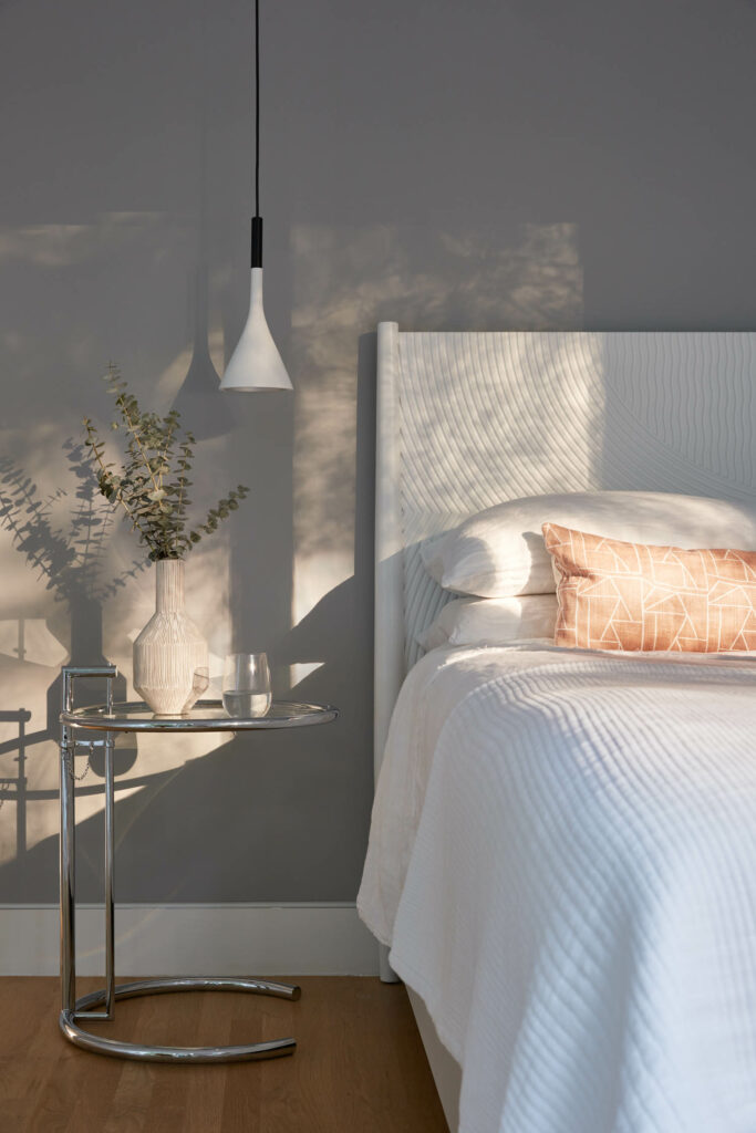 a modern bedroom with white linens on the bed and a pendant at the bedside