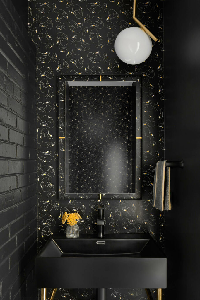 a moody powder room with black painted brick and matching black and yellow wallpaper