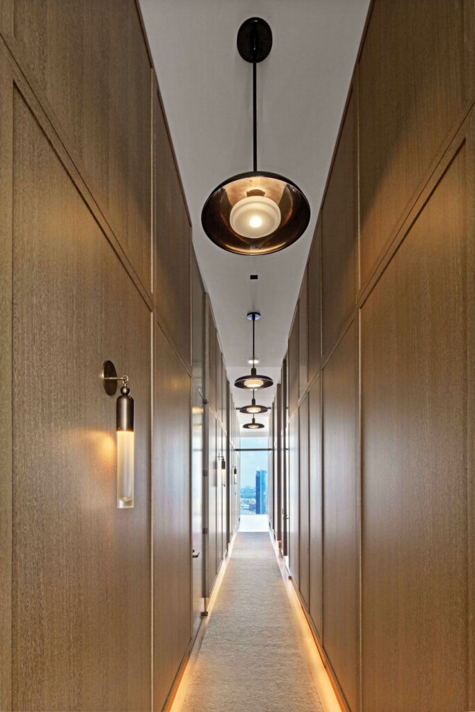 the center hallway of an apartment with tubular sconces and hanging pendants