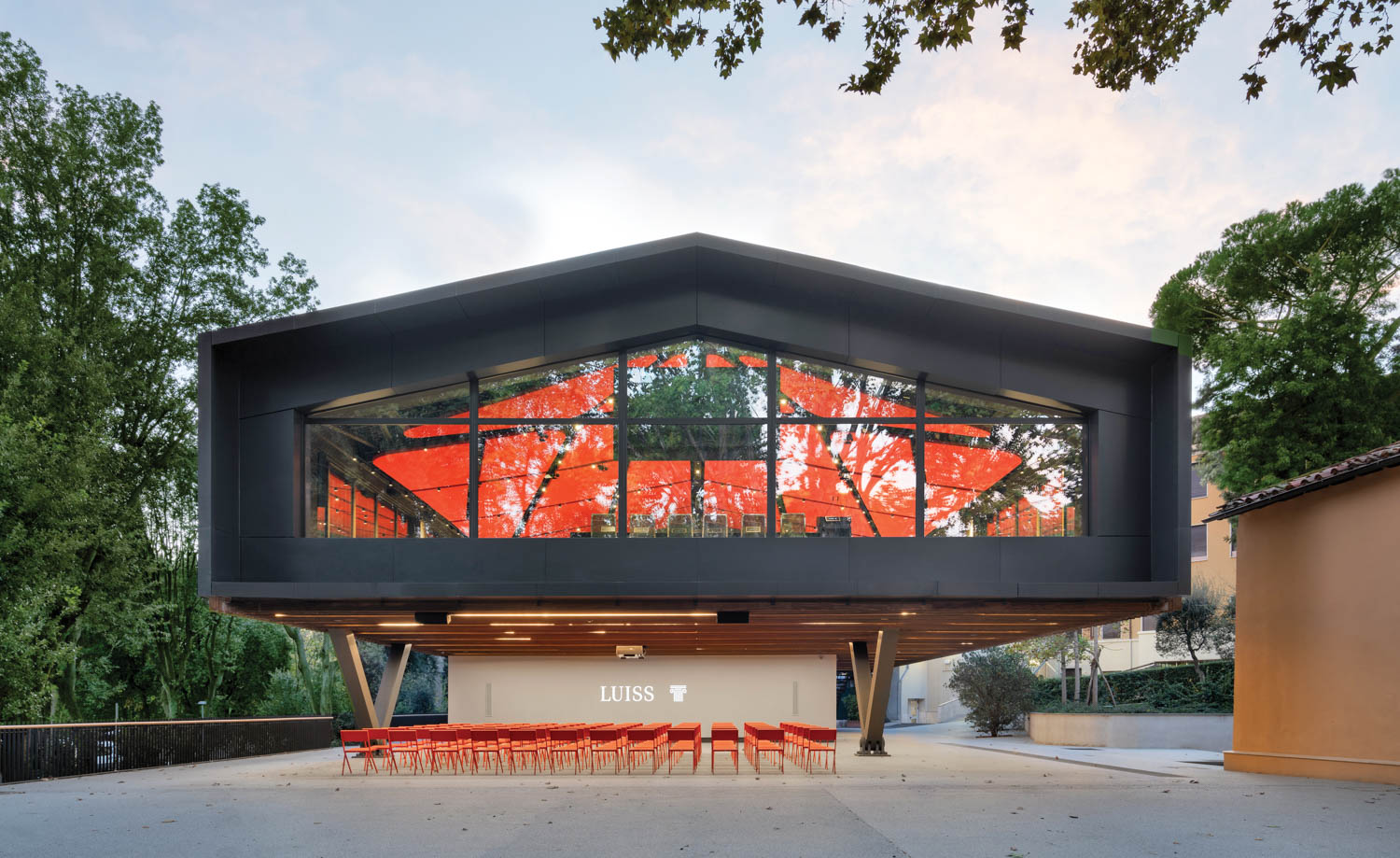 rows of red seating outside match the acoustic panels seen through the windows of this amphitheater