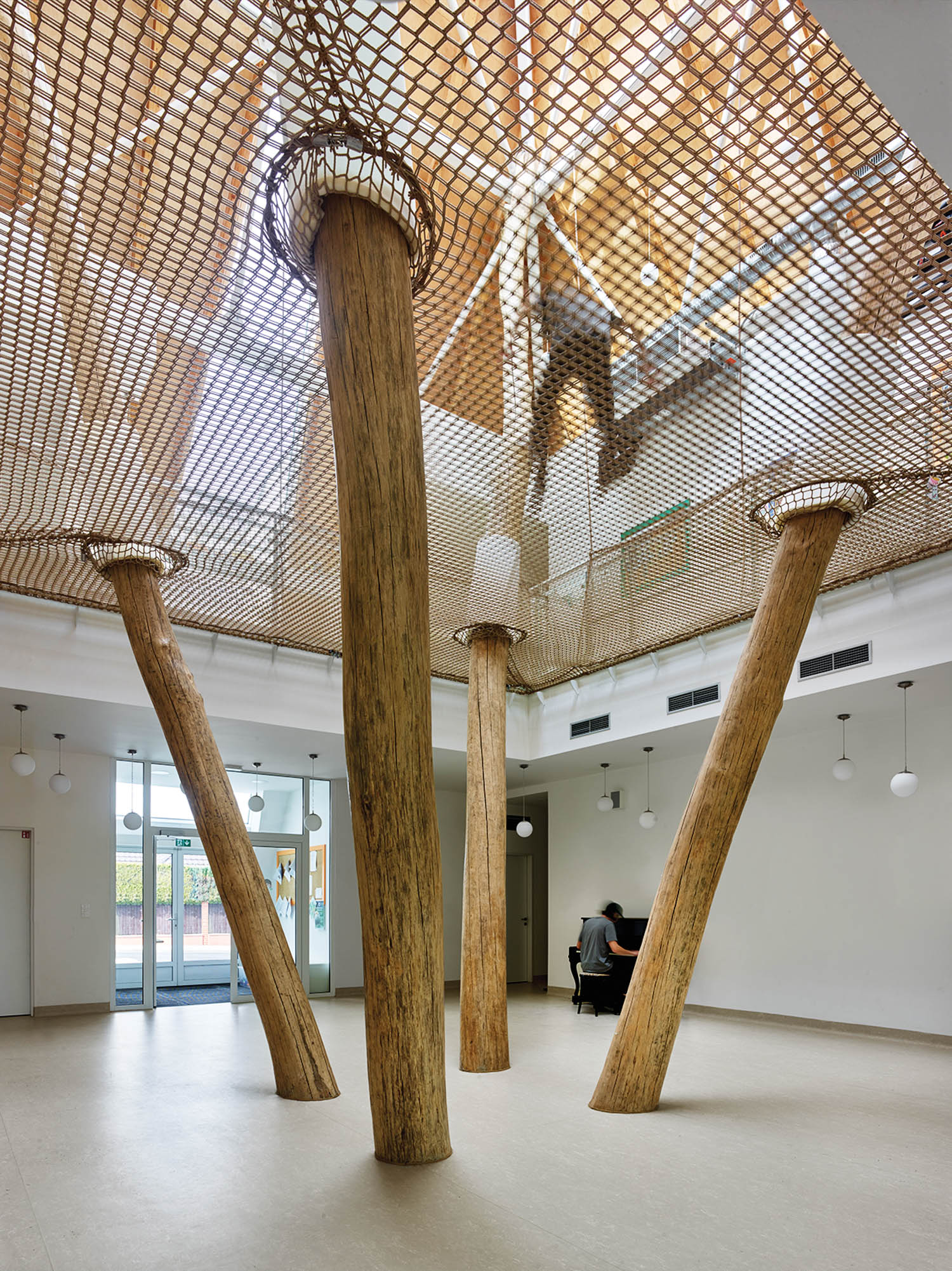 angled tree trunks push through a rope climbing area inside a primary school