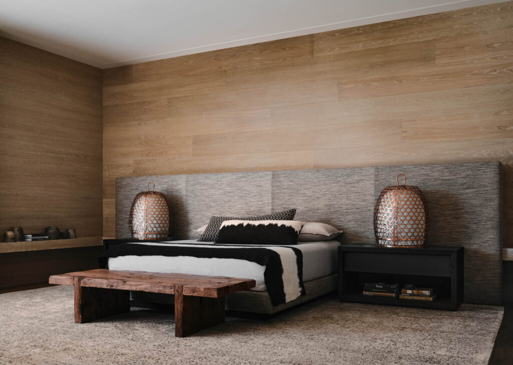 a primary bedroom with a grey upholstered wall-length headboard against wood paneling