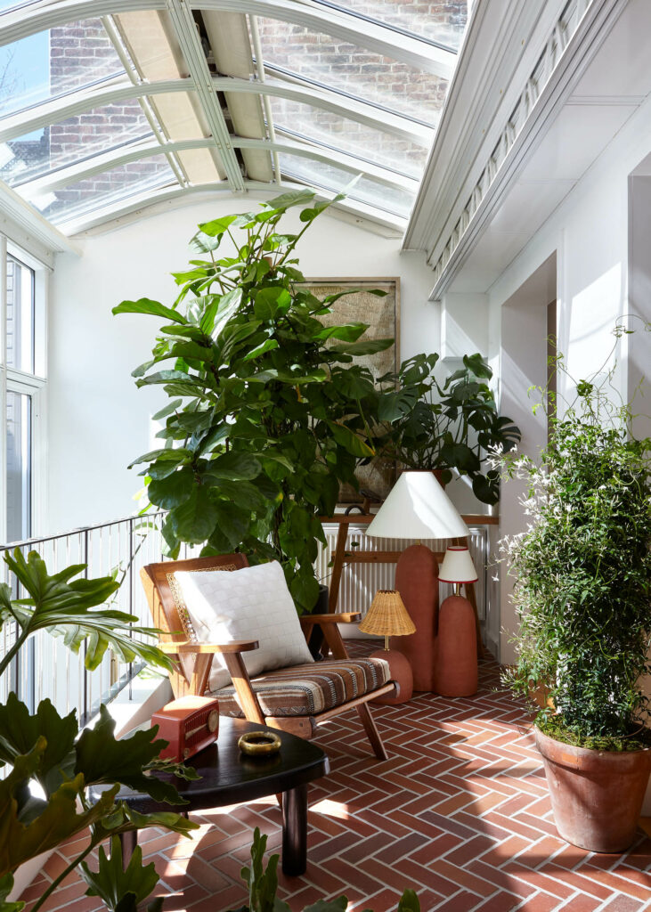 a home's conservatory with large plants and teak lounge chairs