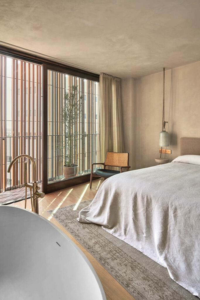 a freestanding tub sits across from a bed and armchair in this penthouse