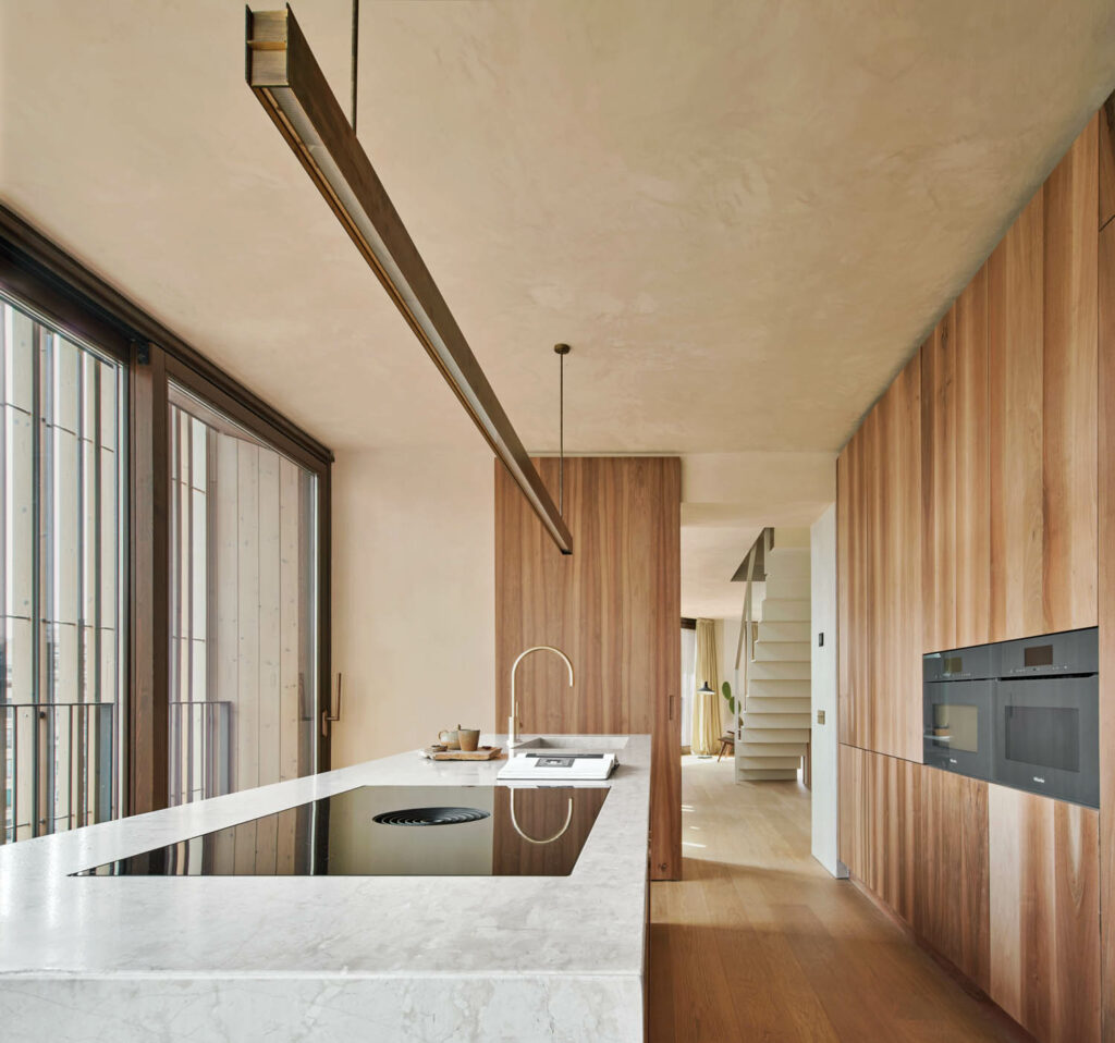 a pendant light hangs over a kitchen island in the room wrapped in French walnut