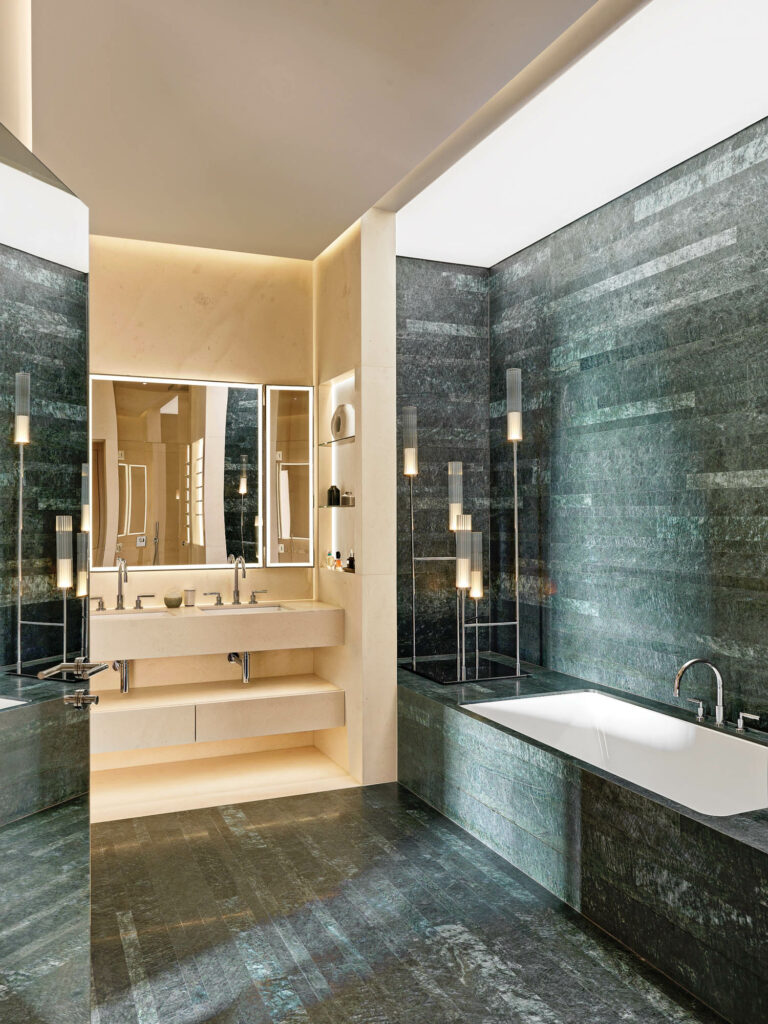 green serpentine stone wraps around the tube area in this apartment's main bathroom