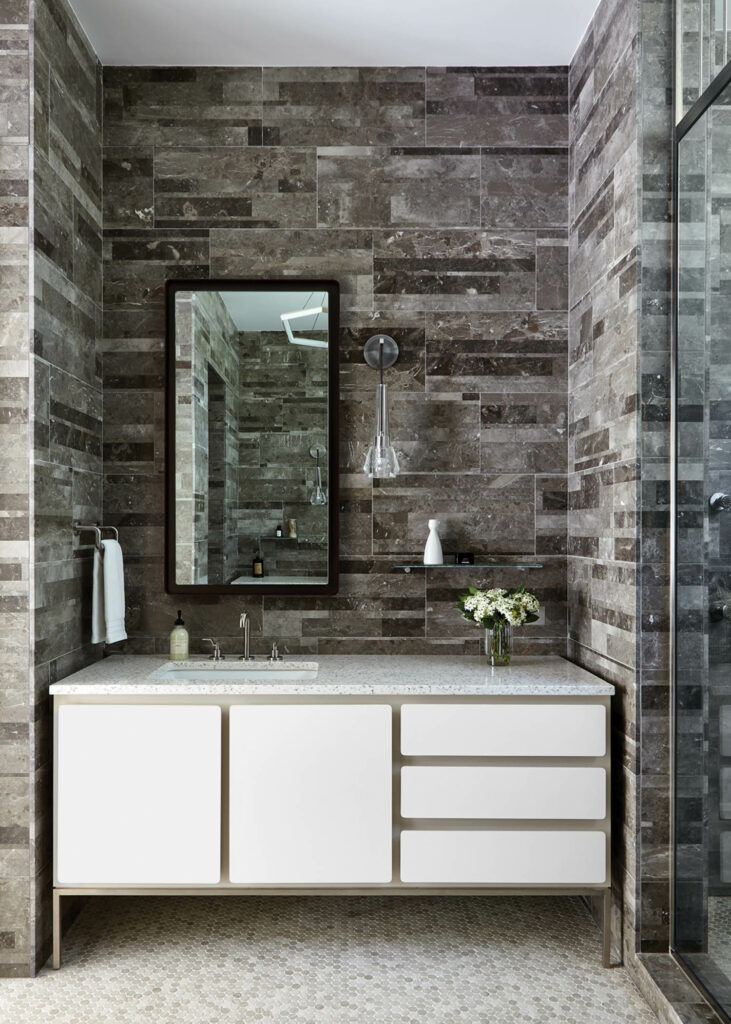 dark marble tile lines the walls of the main bathroom in this home