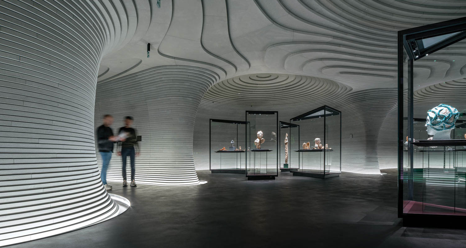 Two people stand in an underground gallery with sloping ceilings