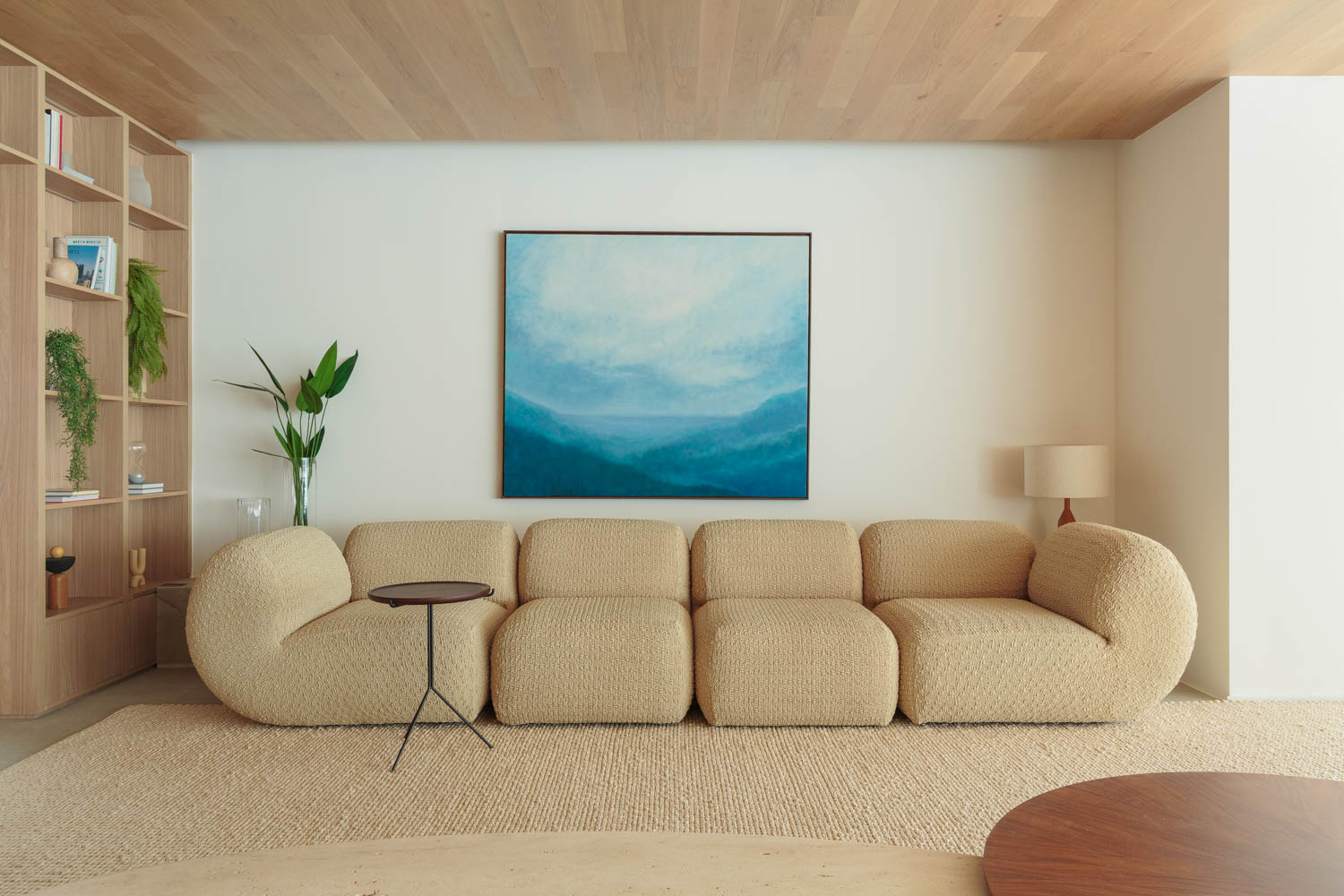 A tan couch that sits on the floor with a blue painting above it