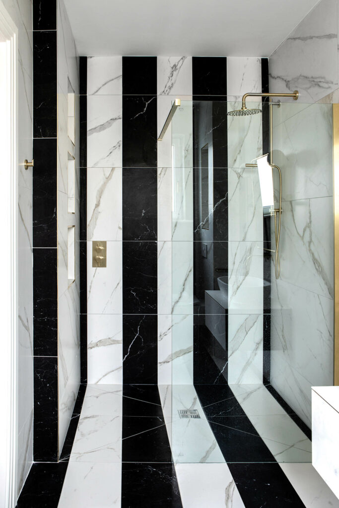 Art deco-inspired stripes of marble tile on the wall and floor of a guest room bath