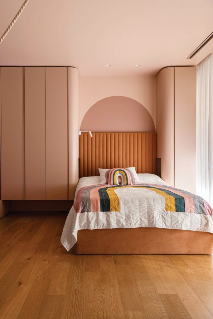 In a daughter’s bedrooms, a built-in wardrobe frames a linen-covered headboard, both custom.